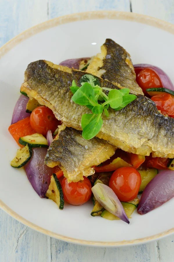 Biban de mare cu legume la tigaie în farfurie