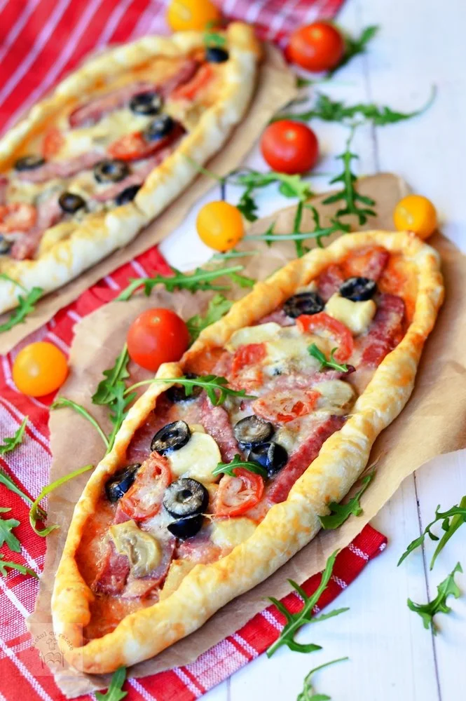 Pizzette cu salam servite pe o farfurie, garnisite cu verdeață proaspătă.