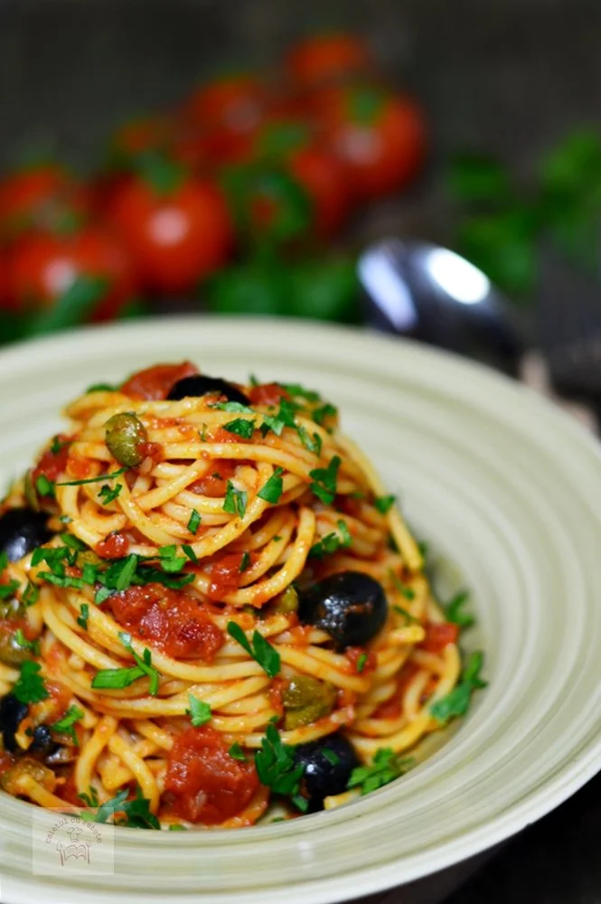 Spaghete alla puttanesca servite cu roșii, măsline și anșoa.